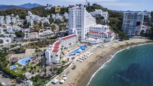 Vista aérea de un complejo turístico costero con varios edificios, una playa y una gran piscina.