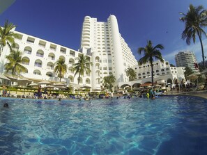 A hotel with a swimming pool, palm trees, and a large building with multiple balconies.