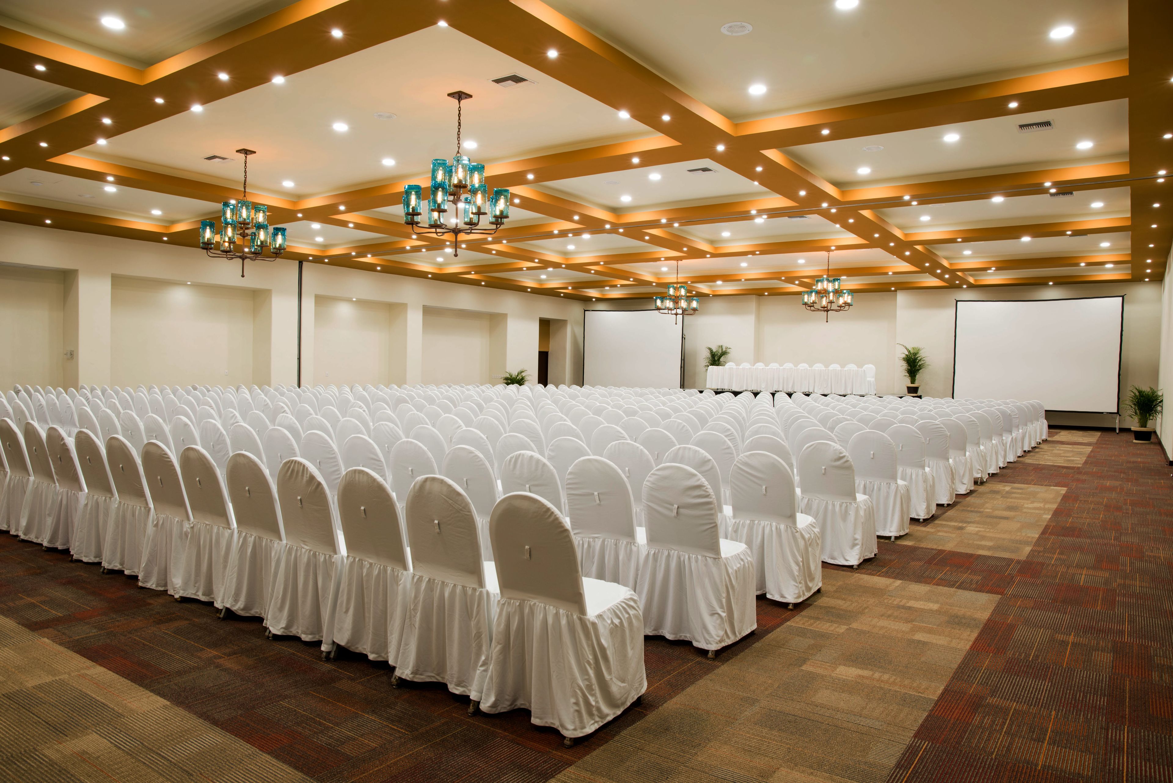 Une grande salle de conférence avec des rangées de chaises blanches, des lustres et un sol recouvert de moquette.