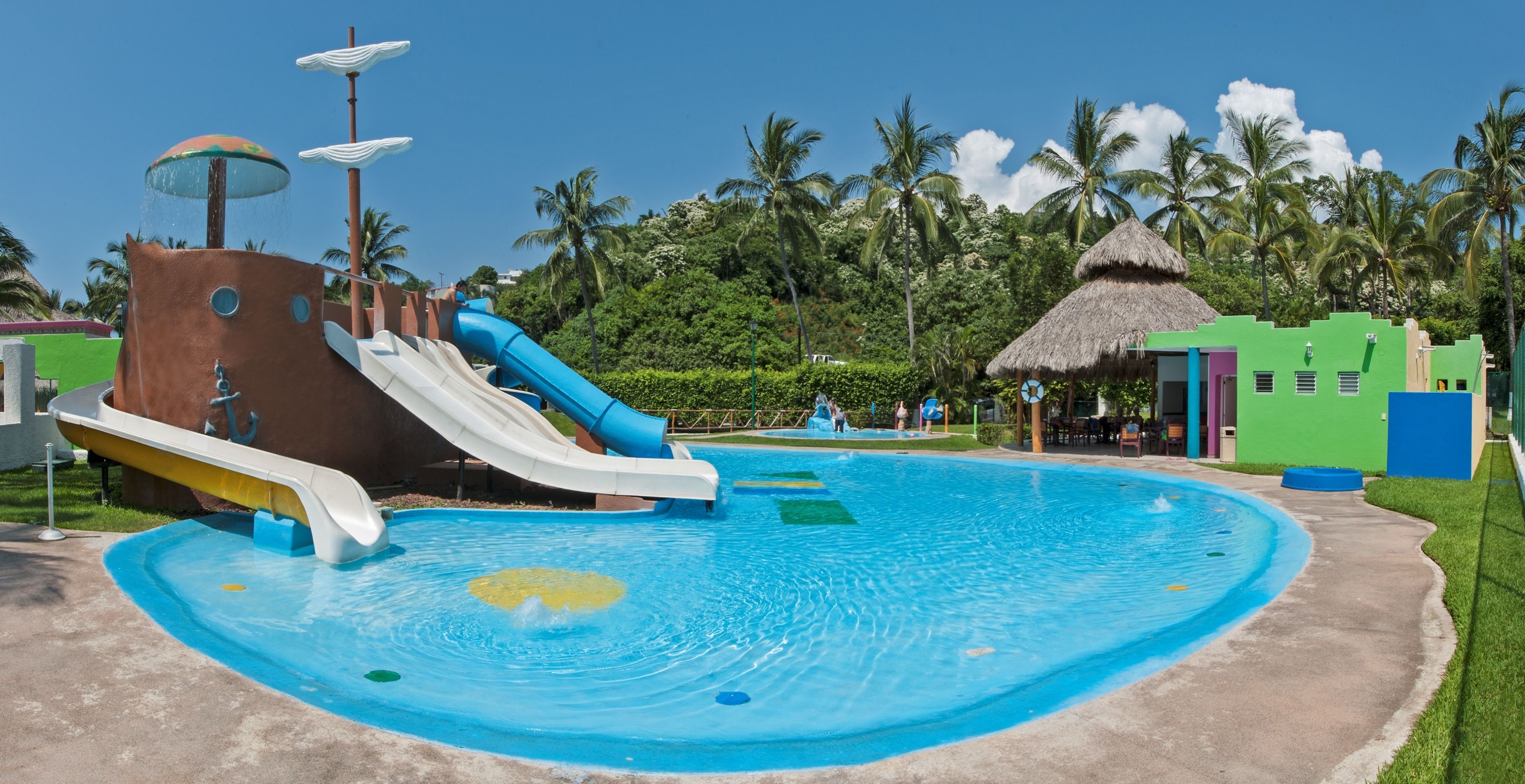 Parque acuático con una piscina grande, toboganes y una cabaña de techo de paja.