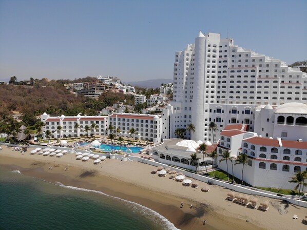A resort with a large pool, beach, and multiple white buildings.