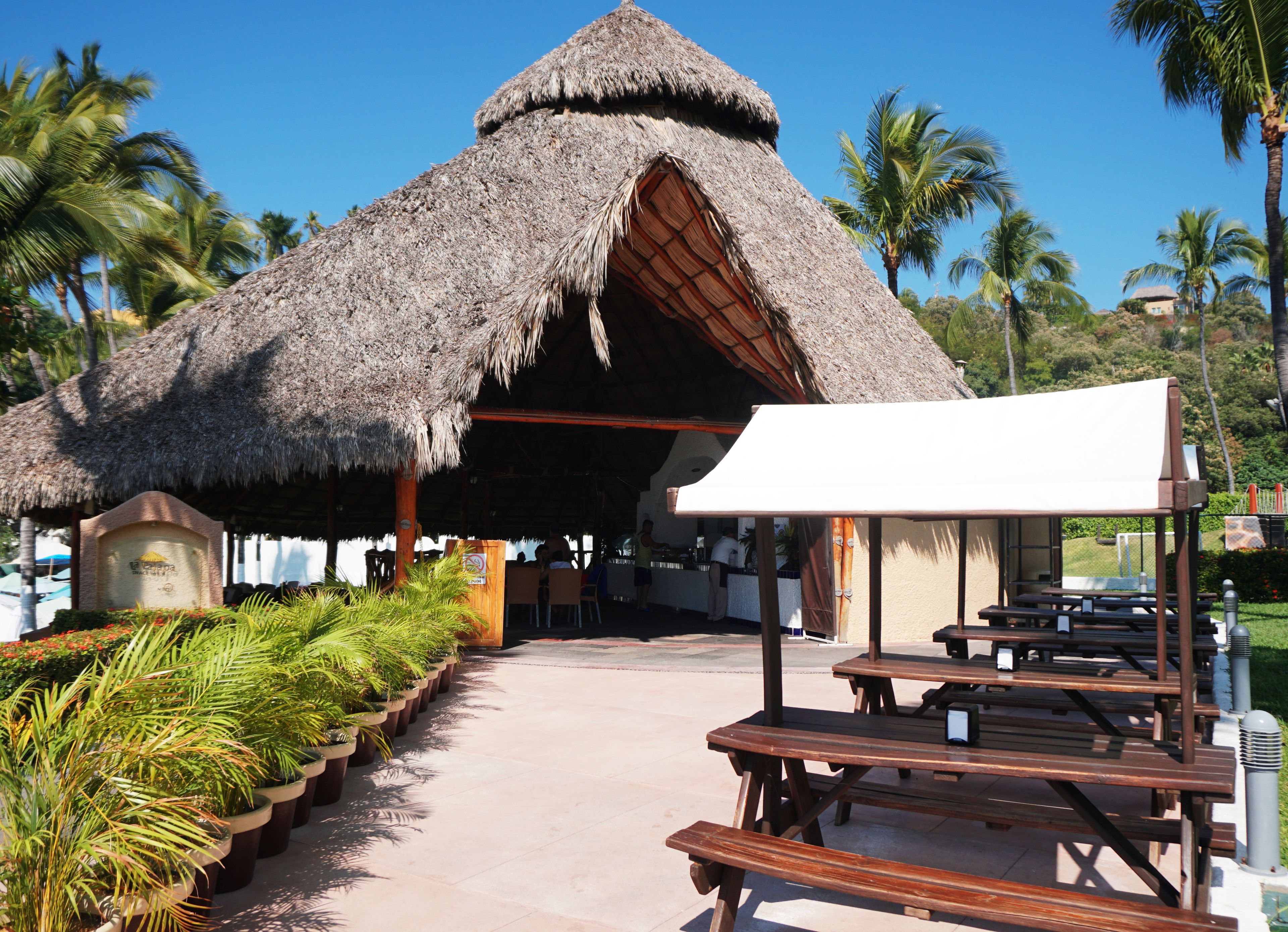 A thatched-roof structure with outdoor seating and a paved walkway.