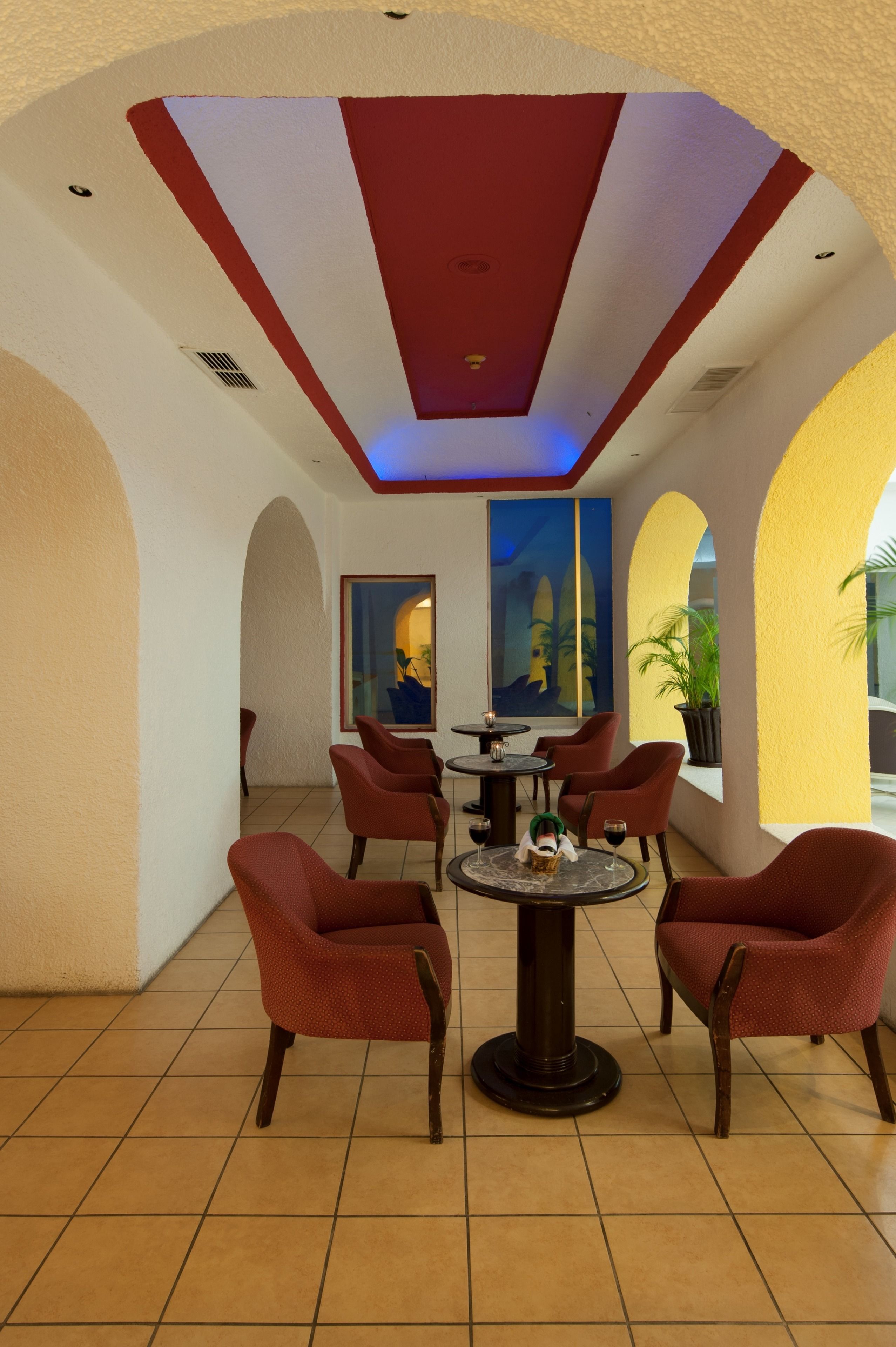 Un hall d’entrée avec des fauteuils rouges, une table ronde et un plafond éclairé de couleurs rouge et bleue.