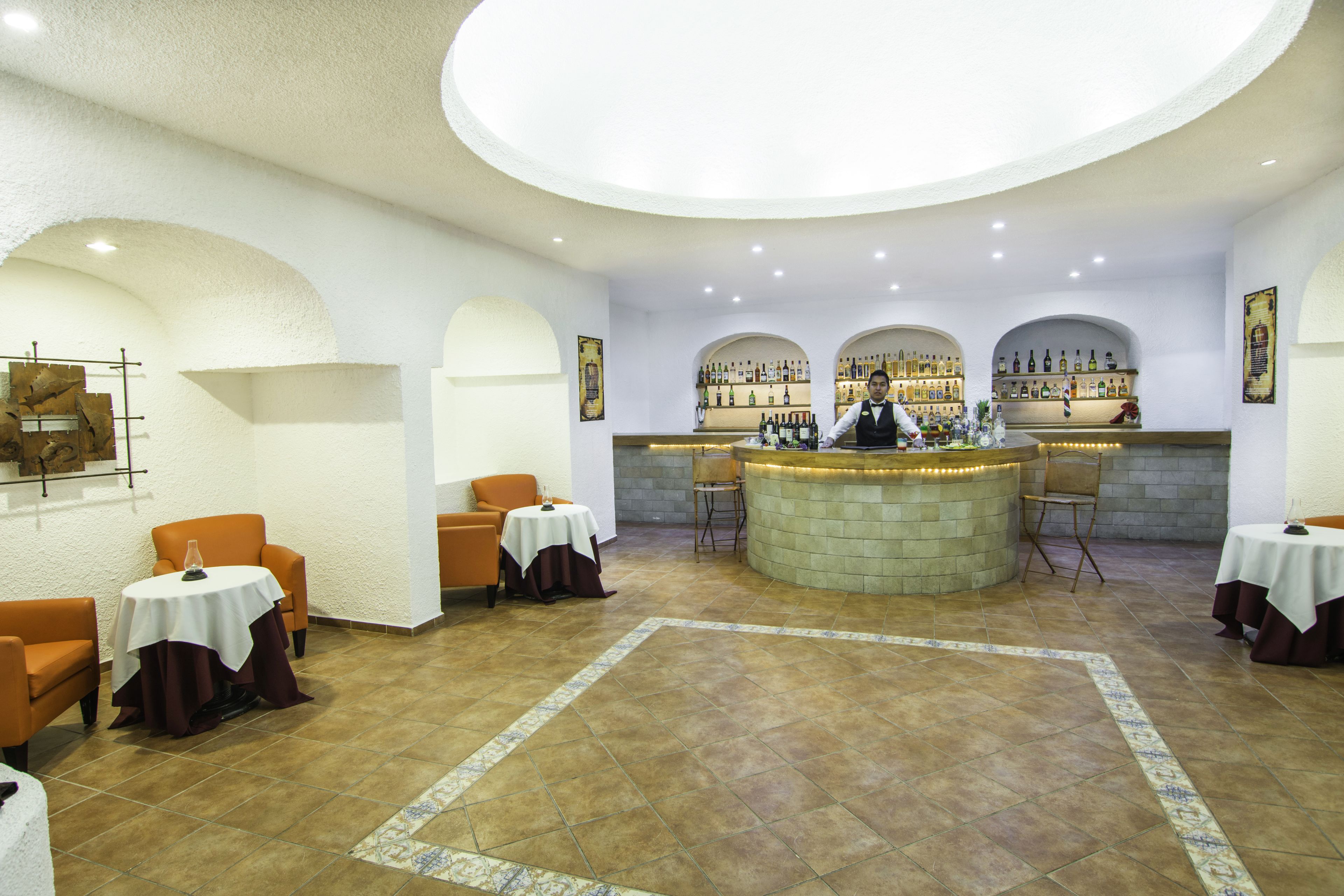 A bar area with a curved counter, multiple seating options including round tables and chairs, and a tiled floor.