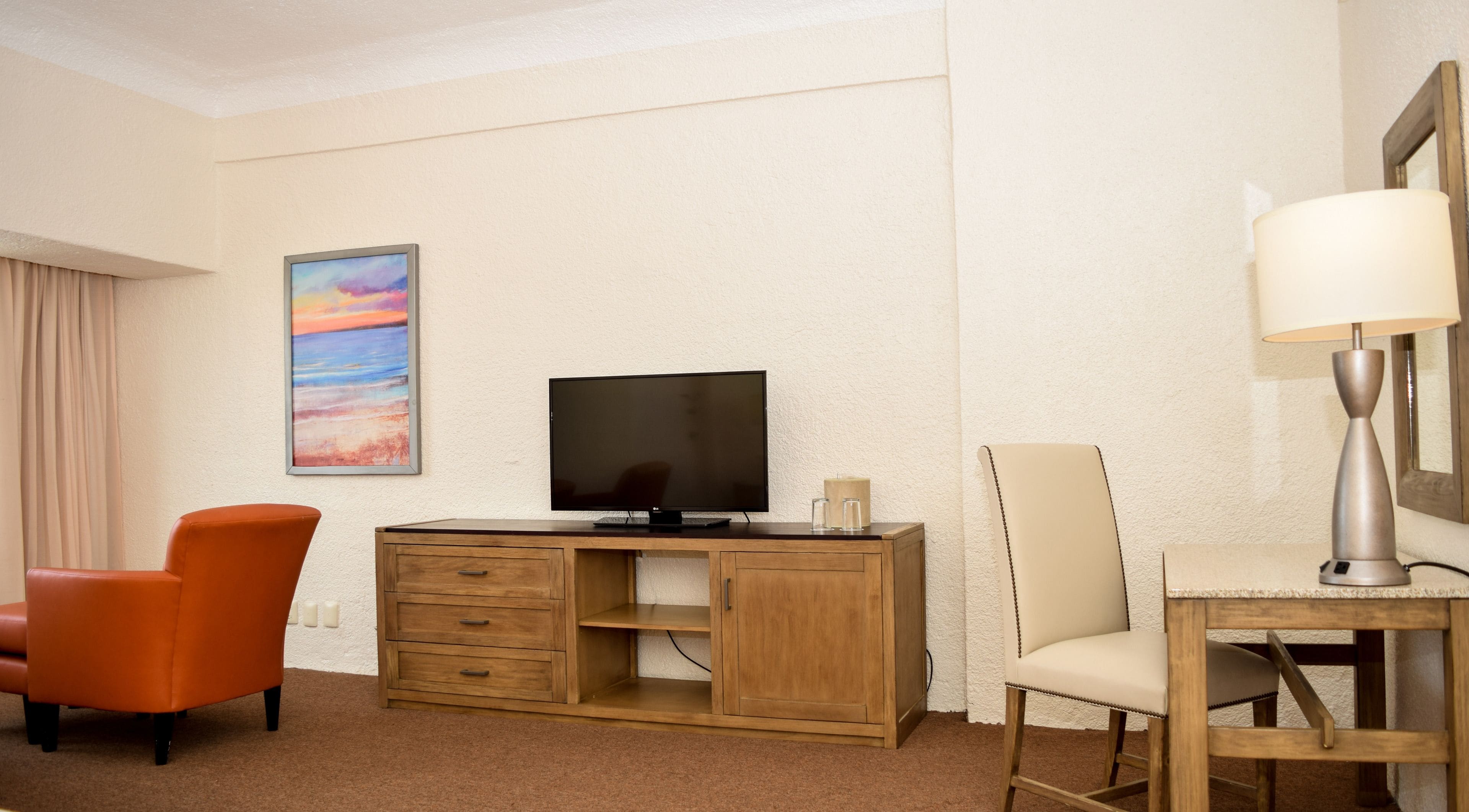 Una habitación de hotel con un escritorio de madera, televisor, silla y lámpara.