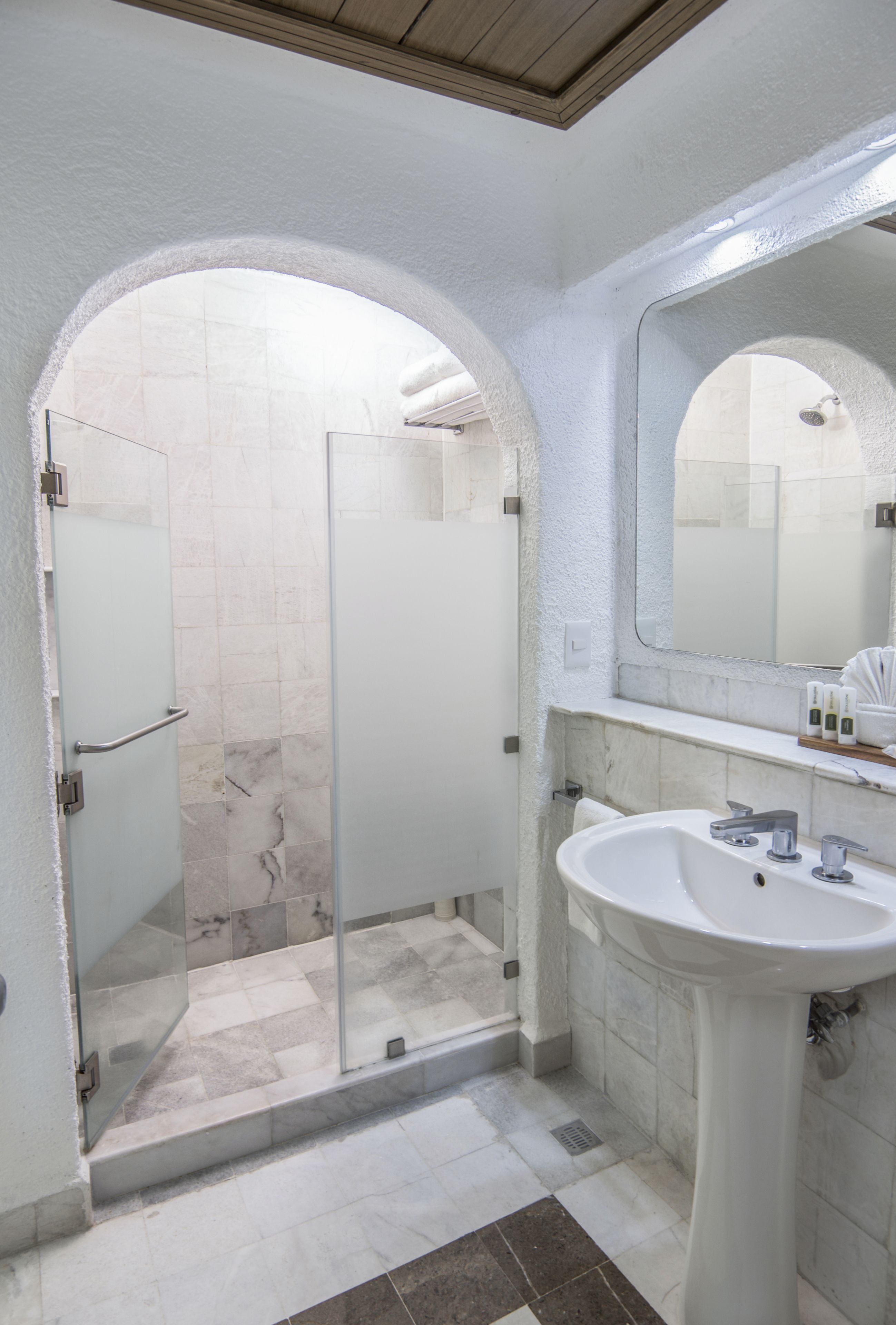 Ein Badezimmer mit einer gläsernen Duschkabine, einem weißen Waschbecken und einem marmorbodenbelagten Boden.