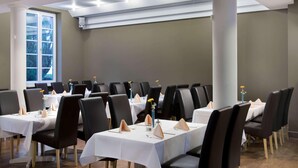 Une salle de conférence avec des tables disposées pour les réunions, équipée de chaises et de tables, et une grande fenêtre laissant entrer la lumière naturelle.