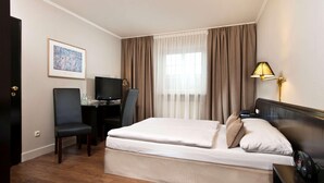 Une chambre d’hôtel comprenant un lit, un bureau avec une chaise, une télévision, une lampe et un tableau encadré au mur.