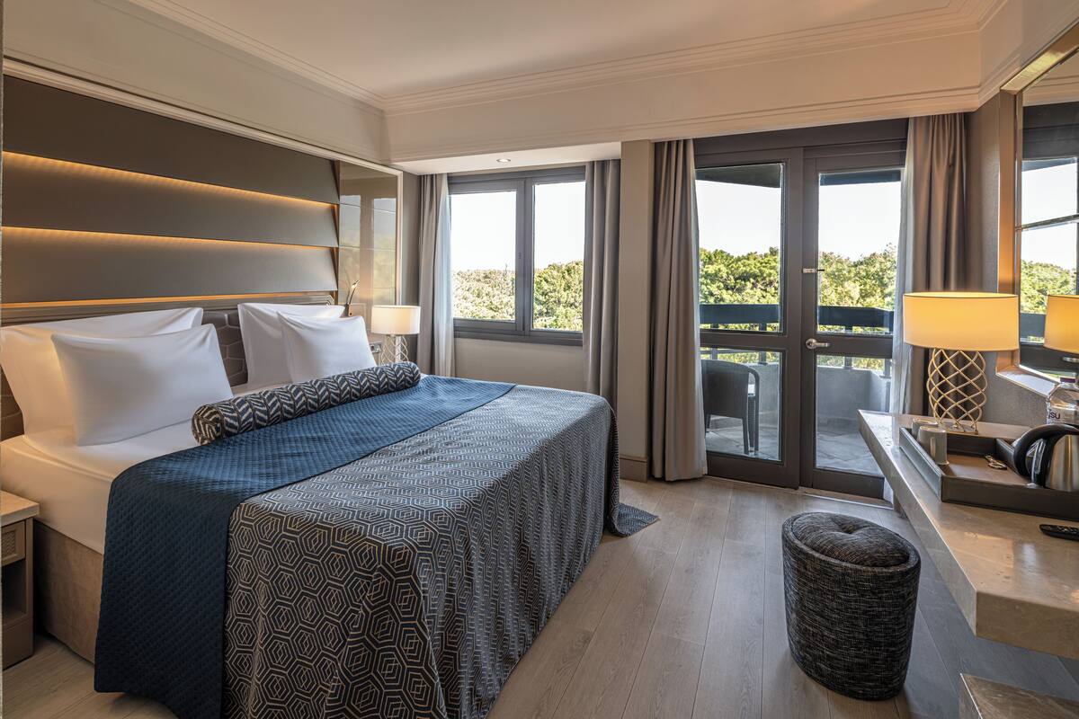 Quarto de hotel moderno com uma cama grande, um espaço de estar pequeno e uma varanda com vista.