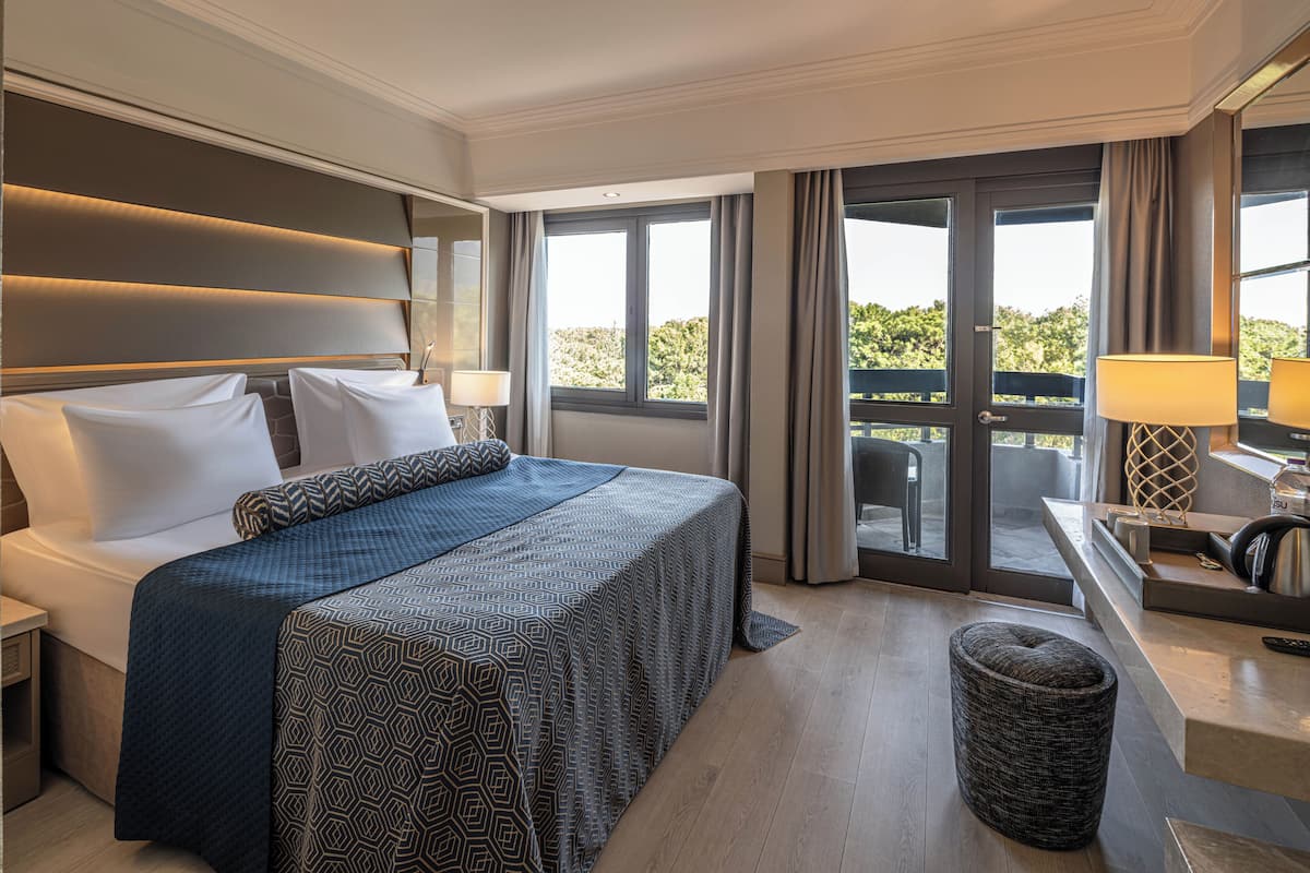 Quarto de hotel moderno com uma cama grande, uma escrivaninha com candeeiro e vista para o exterior.