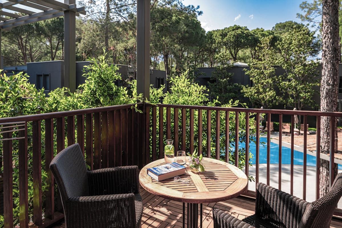 Um deck de madeira com móveis de vime, uma mesa redonda e vista para uma piscina.