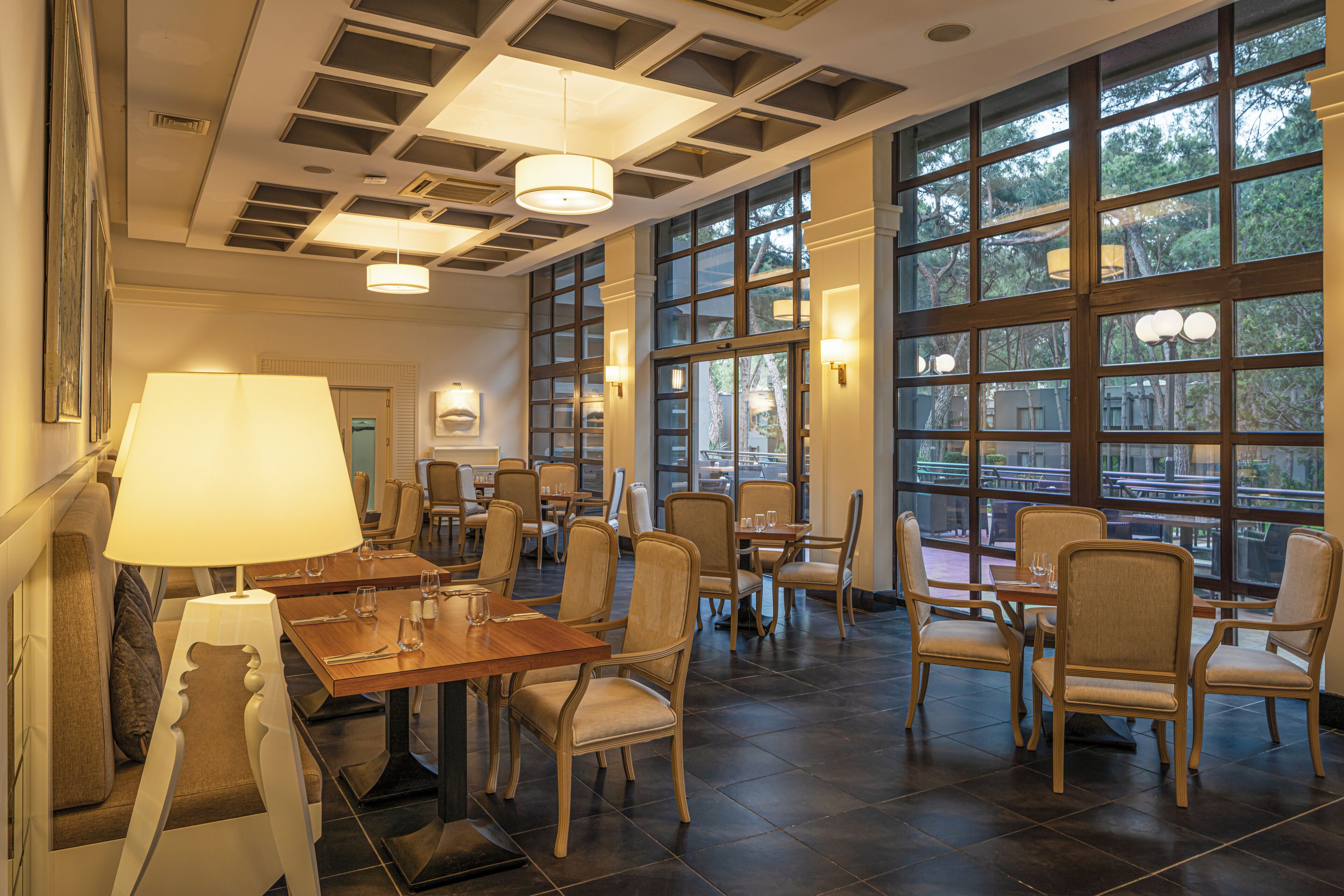 A spacious dining area with multiple tables and chairs, large windows, and modern lighting fixtures.