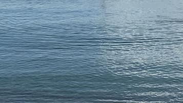 A glass of drink on a ledge with a view of a calm sea and a sailboat in the distance.