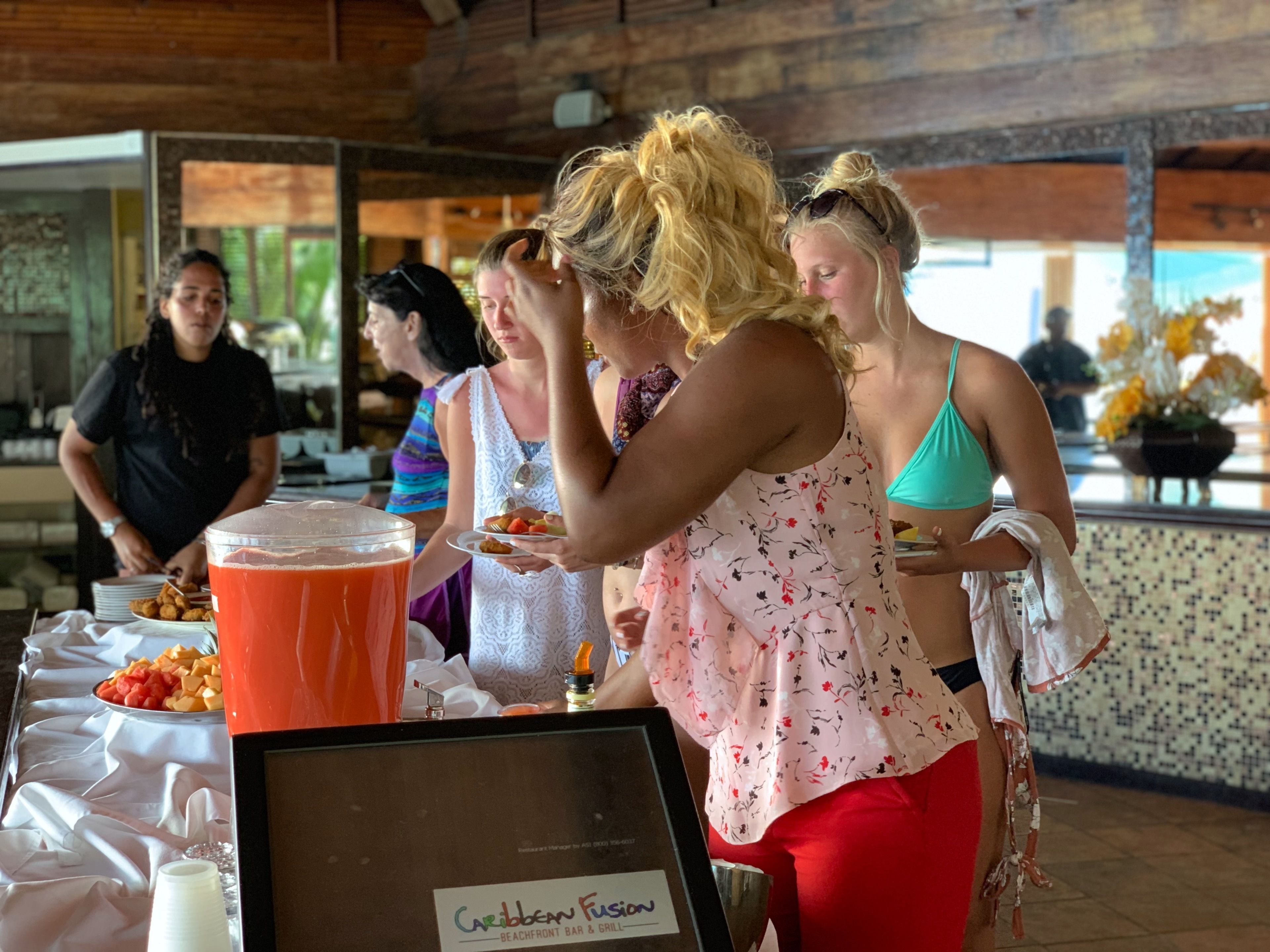 A buffet table with various dishes and a large jug of orange juice.