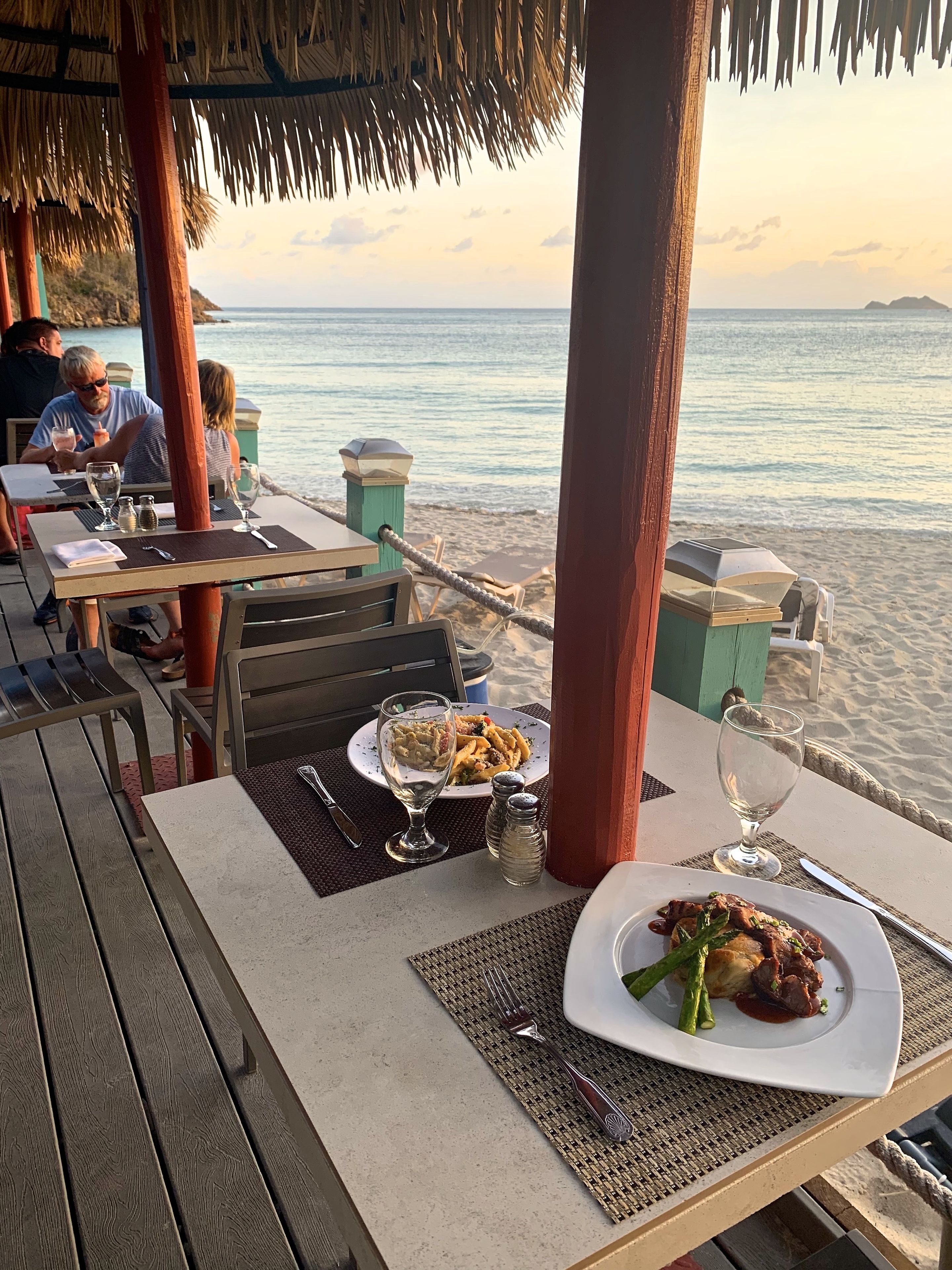 An outdoor dining area with tables and chairs, overlooking a beach and the sea.