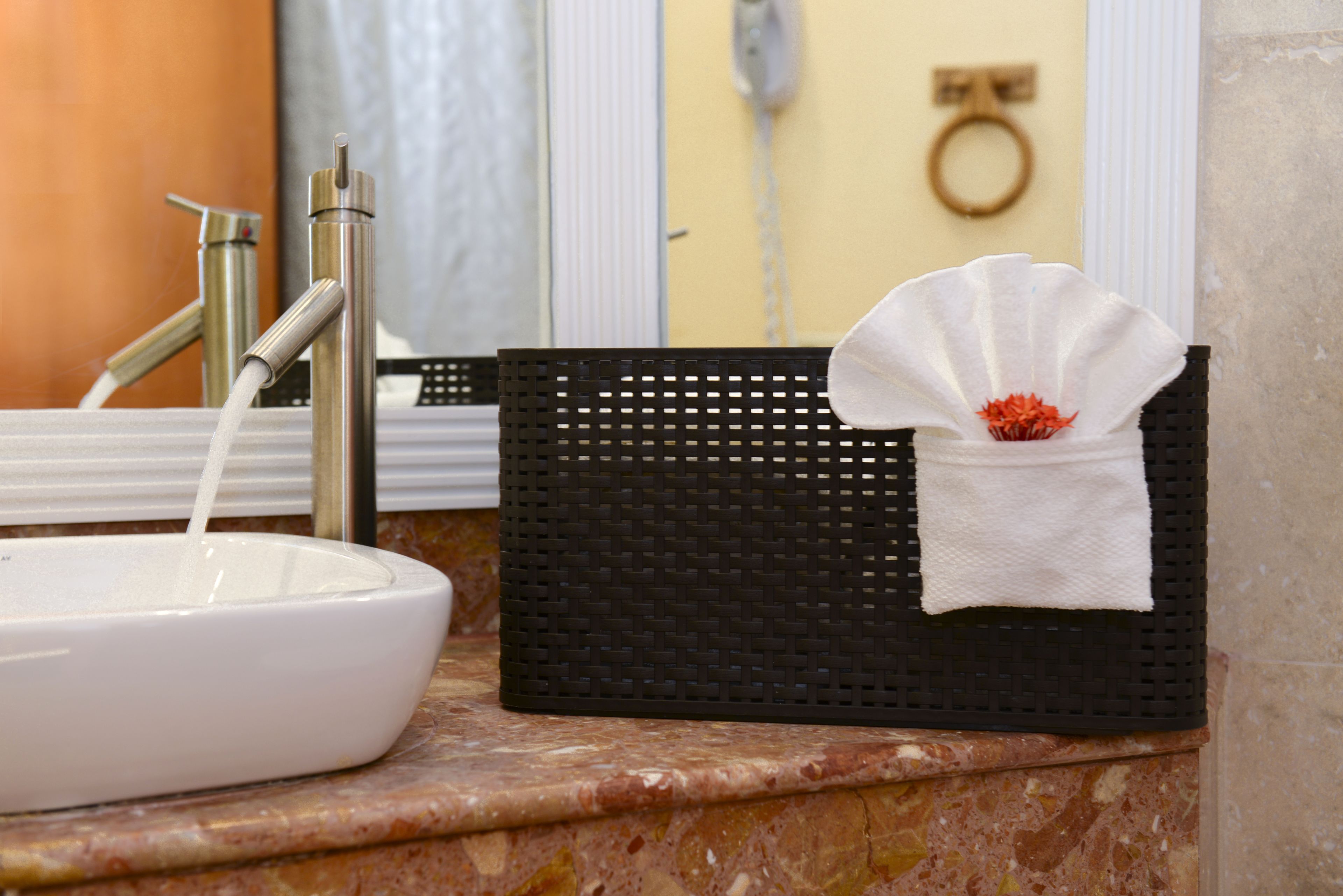 A bathroom sink with a white basin and a black basket with a white towel.