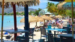 An outdoor seating area with tables and chairs, umbrellas, and a view of the beach and ocean. - Emerald Beach Resort (St. Thomas)