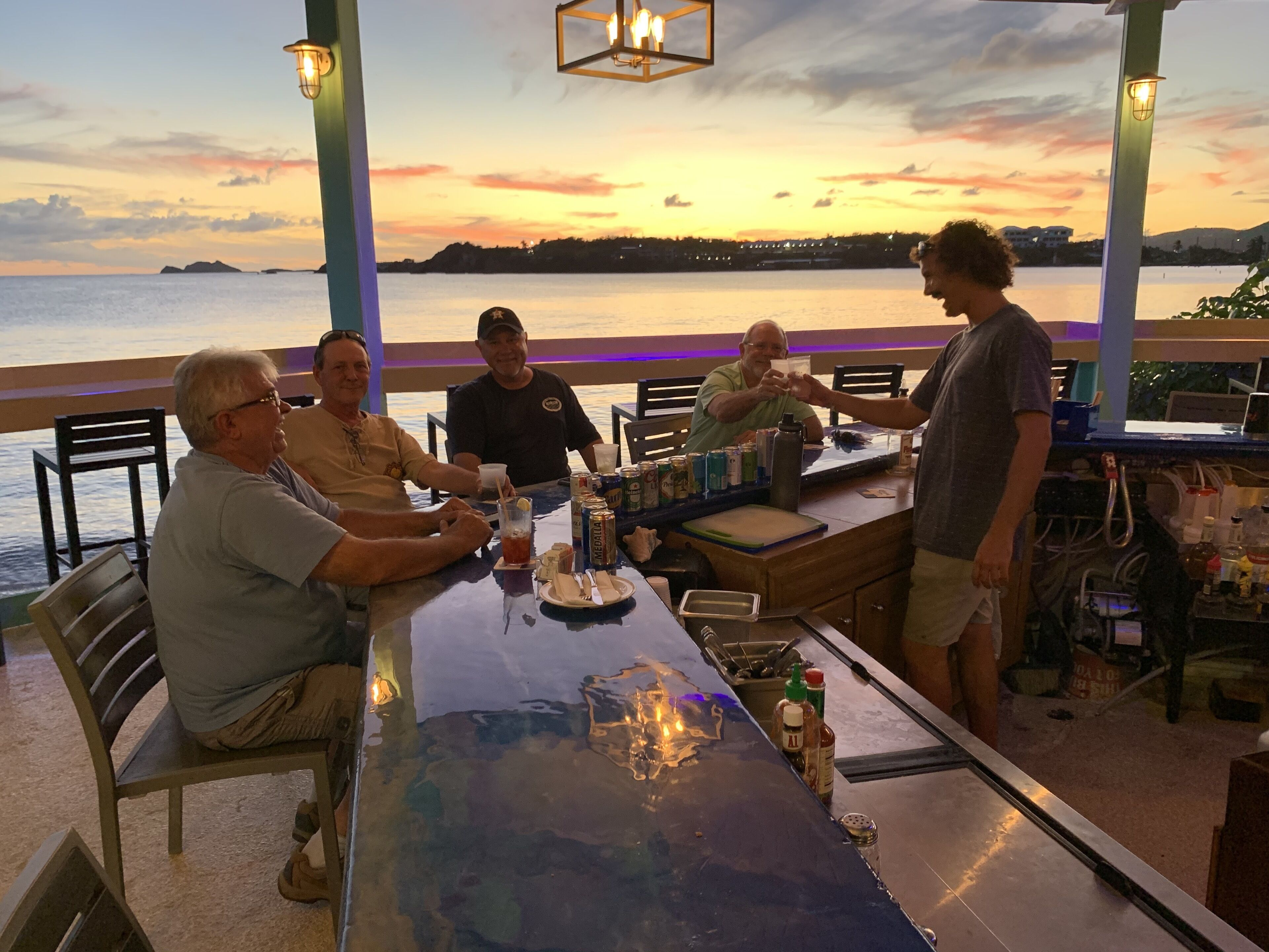 Un grupo de personas sentadas a una mesa con vista al mar durante el atardecer.