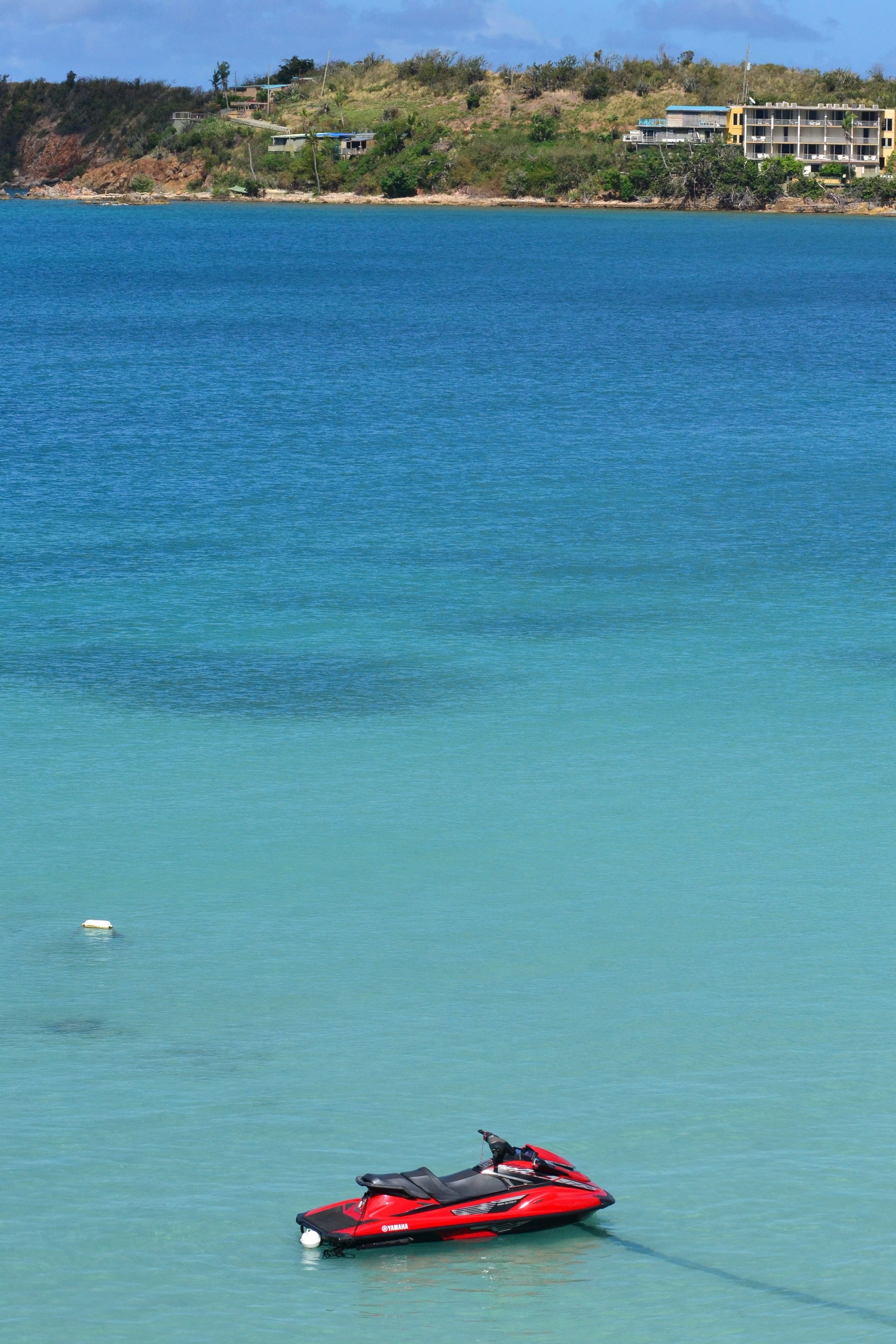 A red jet ski on calm blue water with a coastal landscape in the background.