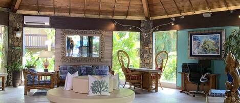 A spacious room with a high ceiling, a ceiling fan, a round seating area, and a dining table.
