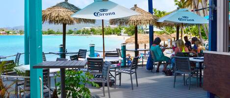 An outdoor patio with tables and chairs, umbrellas, and a view of the beach and ocean.