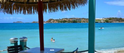 A beachside table with chairs, a thatched roof, and a view of the ocean.
