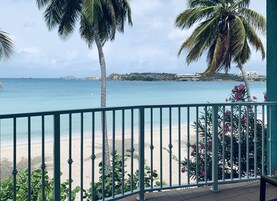 Un balcón con vista a una playa y al océano, con palmeras y barandilla.