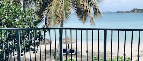 A balcony with a view of a beach, palm trees, and a clear sky.