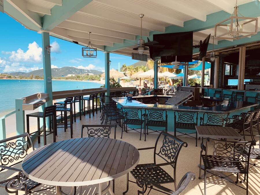 Zona pranzo all'aperto con tavoli e sedie, vista su un corpo d'acqua e una spiaggia.