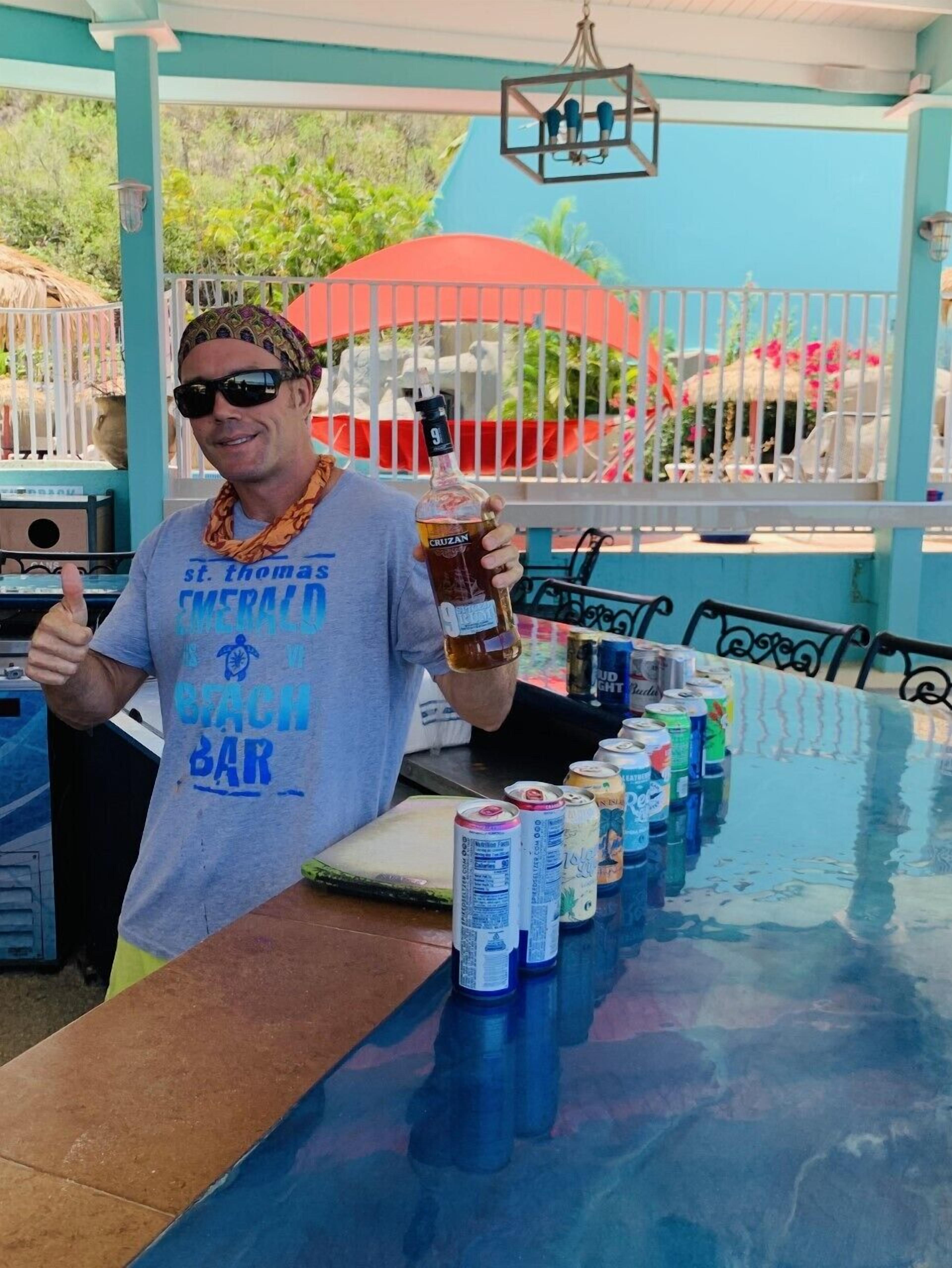 A person at a bar with a drink and cans of beer on the table.