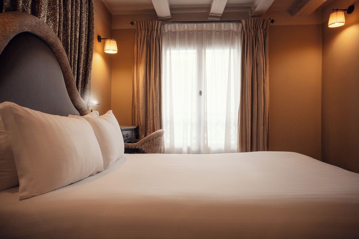 A hotel room with a large bed, a nightstand, a chair, and a window with curtains.