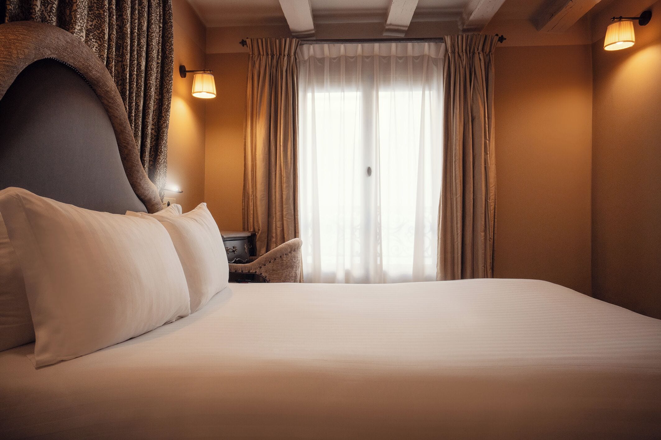 A hotel room with a large bed, a nightstand, a chair, and a window with curtains.