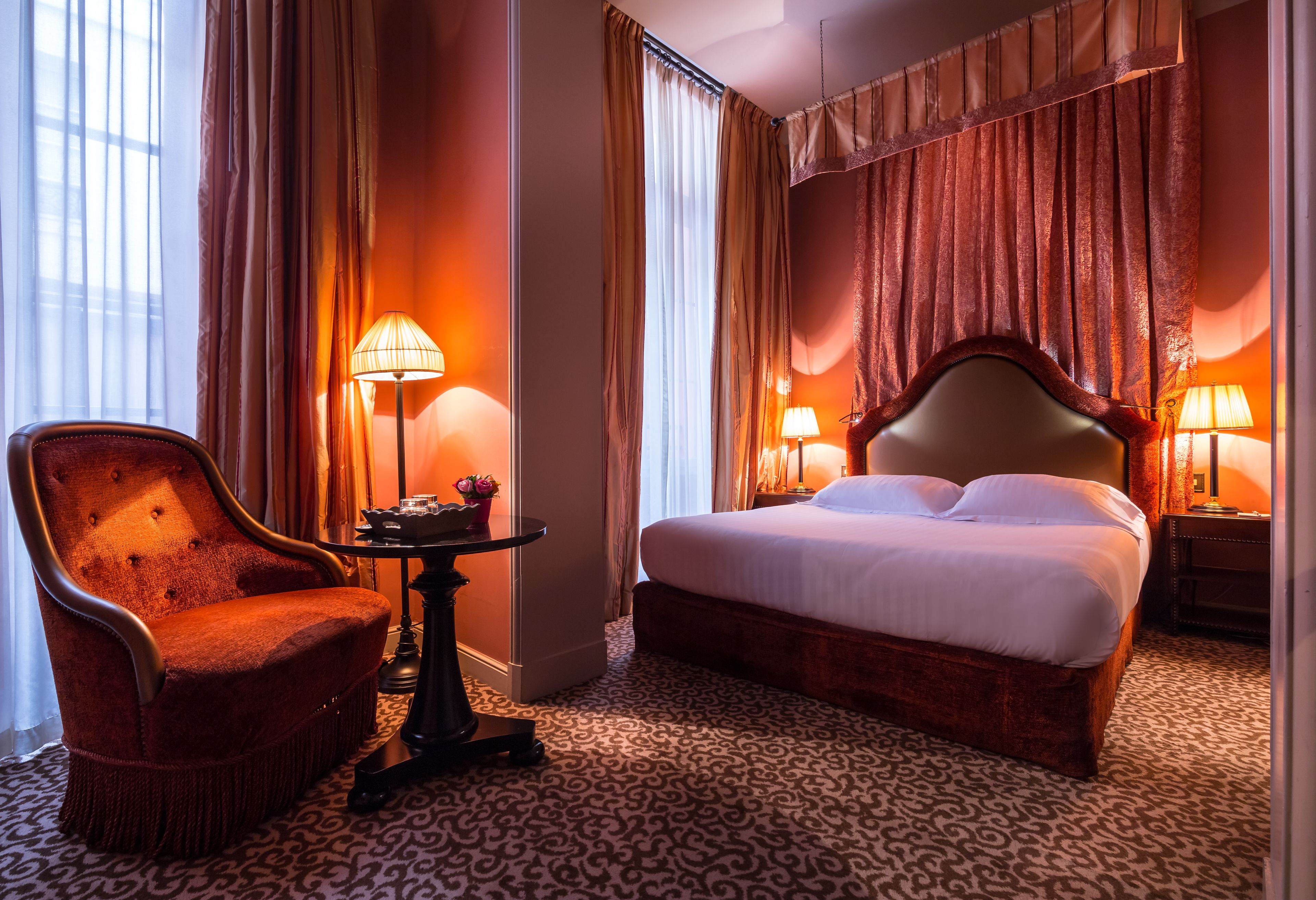 Quarto de hotel com uma cama grande, uma cadeira, uma mesinha e duas luminárias.