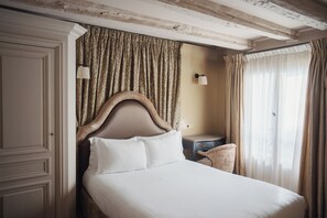 A hotel room with a large bed, a nightstand, a lamp, and a view of the outdoors. - Hotel Odéon Saint Germain (Paris)