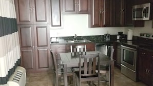 A kitchen with dark wooden cabinets, a dining table with chairs, a microwave, and a stove.