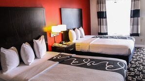 A hotel room with two beds, a nightstand, a lamp, and a view of the outside through curtains.
