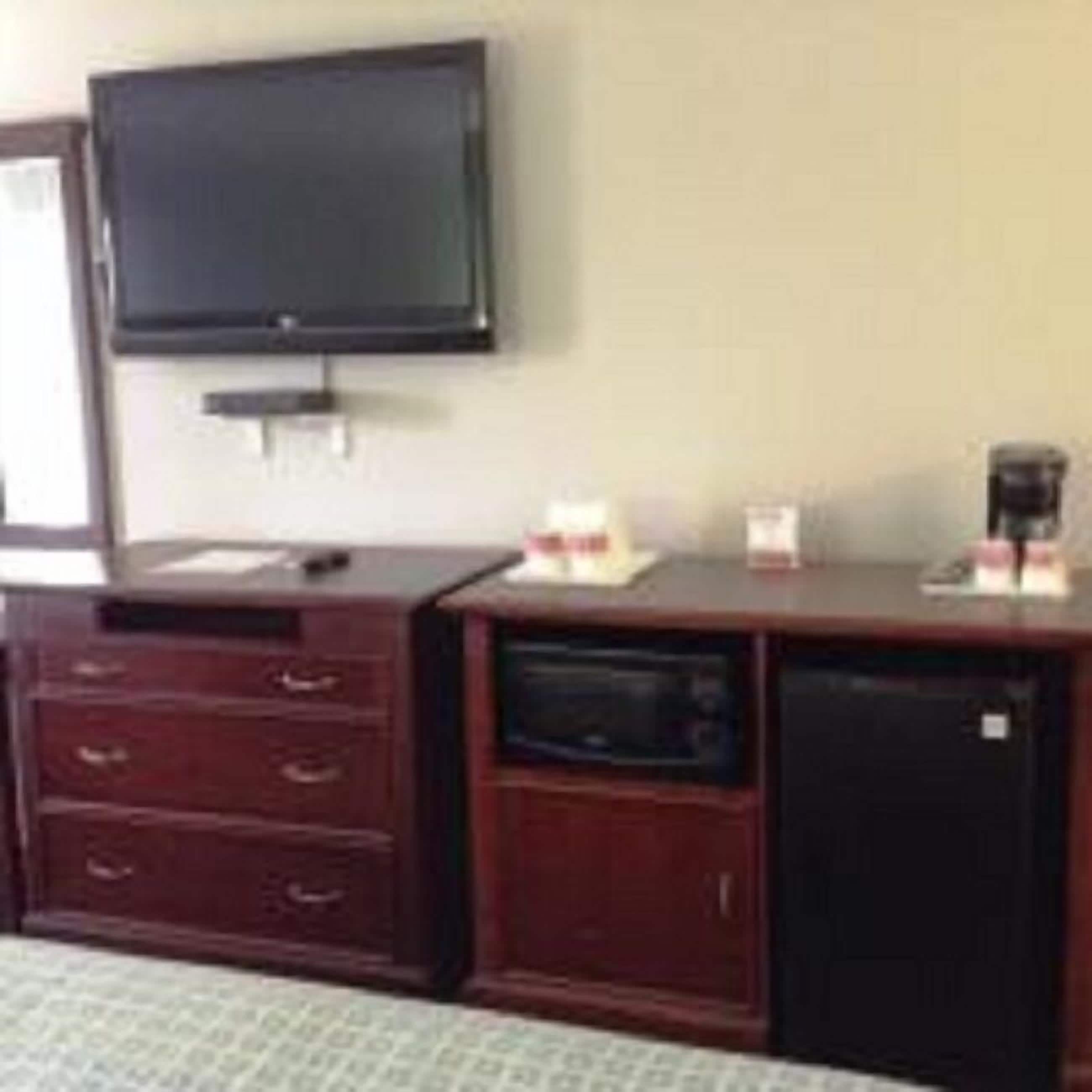Une chambre d’hôtel équipée d’un téléviseur à écran plat fixé au mur, d’une commode en bois avec des tiroirs, d’un four à micro-ondes et d’une machine à café posée sur le comptoir.
