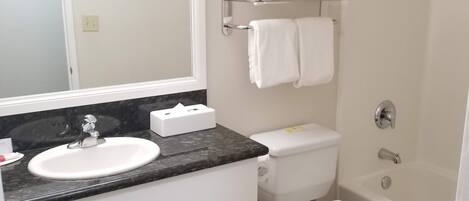 A bathroom with a white sink, mirror, toilet, and bathtub.