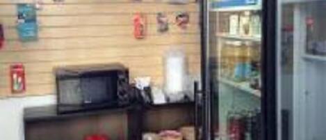 A small retail space with shelves stocked with various packaged goods, a microwave, and a refrigerator.
