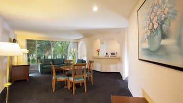 A room with a dining table, chairs, a sofa, a lamp, a painting, and a view of greenery outside.