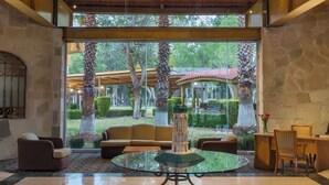 Un vestíbulo espacioso con techo alto, ventanas amplias y vista a un jardín exterior.