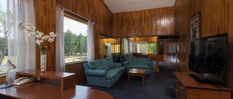 A room with wooden paneling, a blue sofa set, a television, and a desk with a telephone.