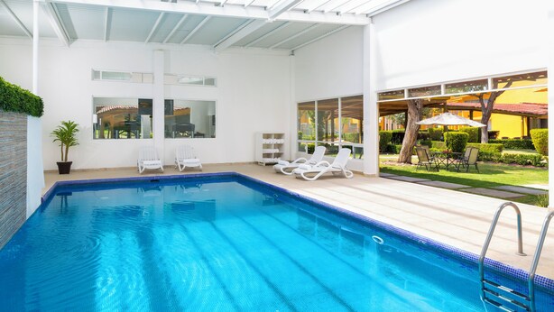 Piscina con sillones de descanso y vista al jardín.