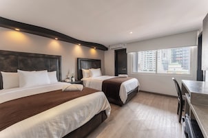 Habitación de hotel con dos camas, un escritorio y ventana con vistas a la ciudad.