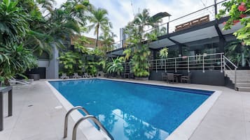 A swimming pool with a clear blue water, surrounded by lush green plants and modern outdoor furniture.