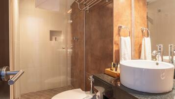 A modern bathroom with a glass-enclosed shower, a white toilet, and a large round sink with a mirror above it.
