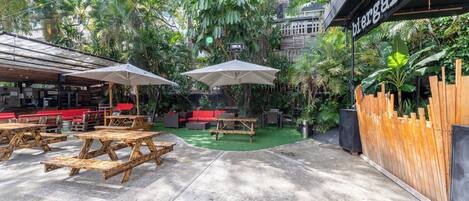 An outdoor seating area with wooden tables and chairs, surrounded by lush greenery and a sign for 'bierstuben'.
