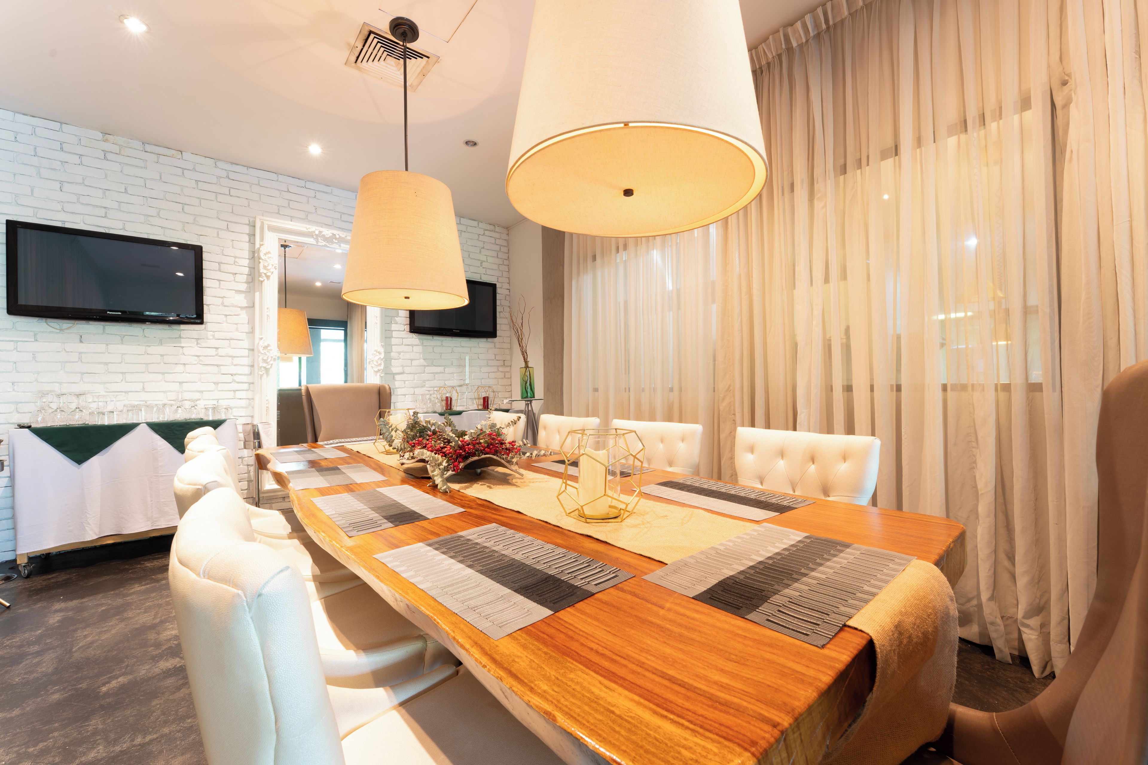A modern dining area with a long wooden table, white upholstered chairs, and a large pendant light.