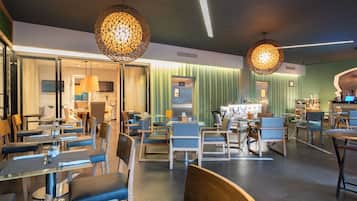Un interior de restaurante moderno con varias zonas de comedor, sillas de madera y lámparas colgantes.