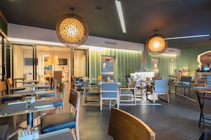 A modern restaurant interior with multiple dining areas, wooden chairs, and hanging pendant lights.